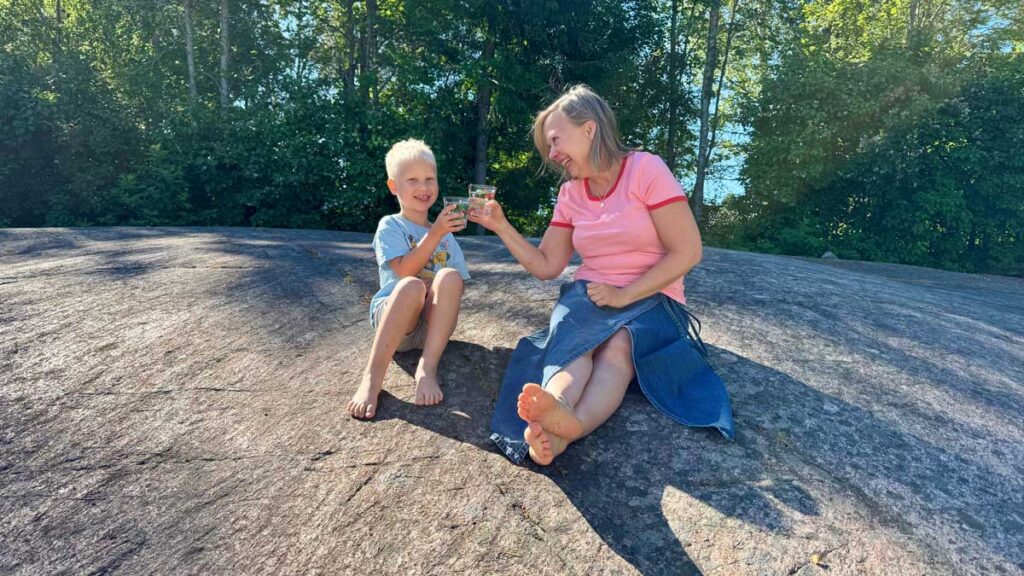 Vuxen och barn som skålar med varsitt glas vatten sittandes på en klipphäll.